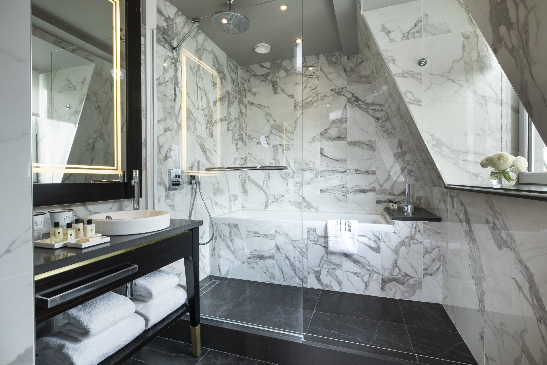Une salle de bain avec murs en marbre et douche à l'italienne.