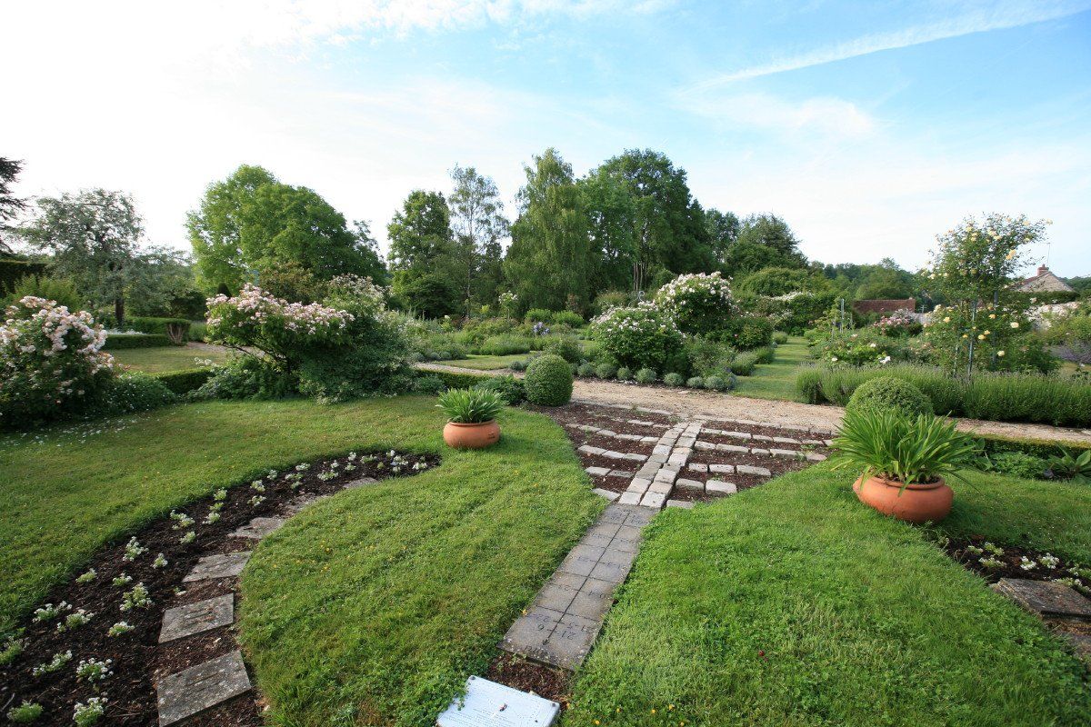 Jardin soigné avec pelouses vertes, marches en pierre et parterres de fleurs en terrasses sous un ciel bleu