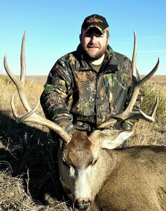 Man in camo with a large buck he has hunted in an open field.