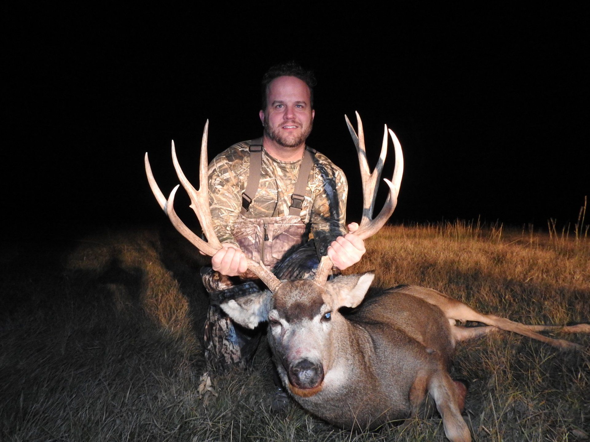Hunter in camouflage holding large buck deer with impressive antlers at night.