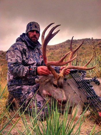 Man in camo with large buck he harvested, outdoors.