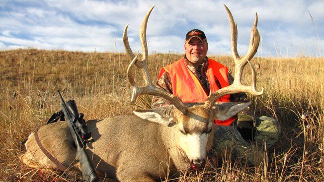 Hunter kneeling next to a large buck with impressive antlers, in a field.