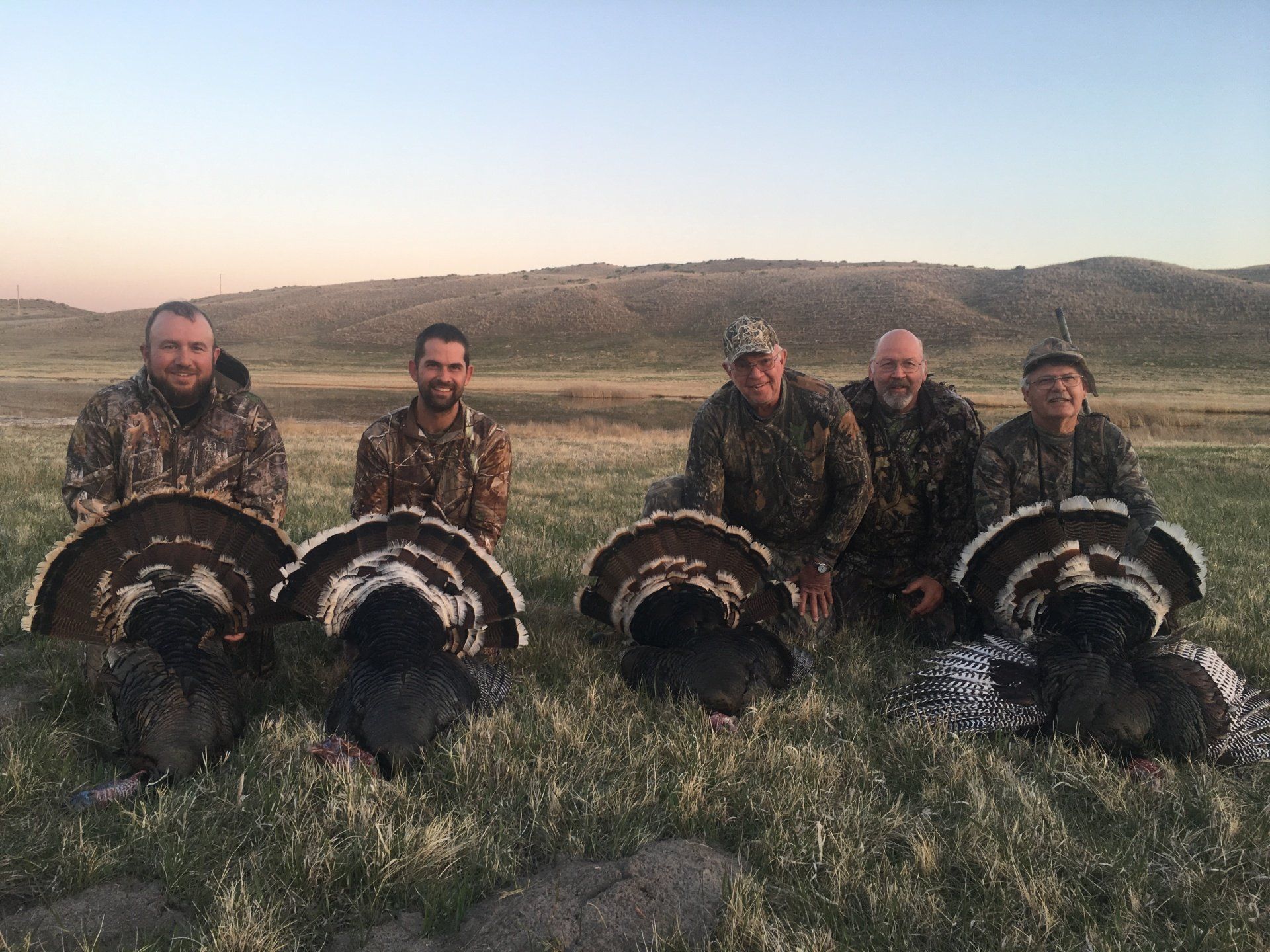 Five hunters pose with turkeys they killed in a grassy field.