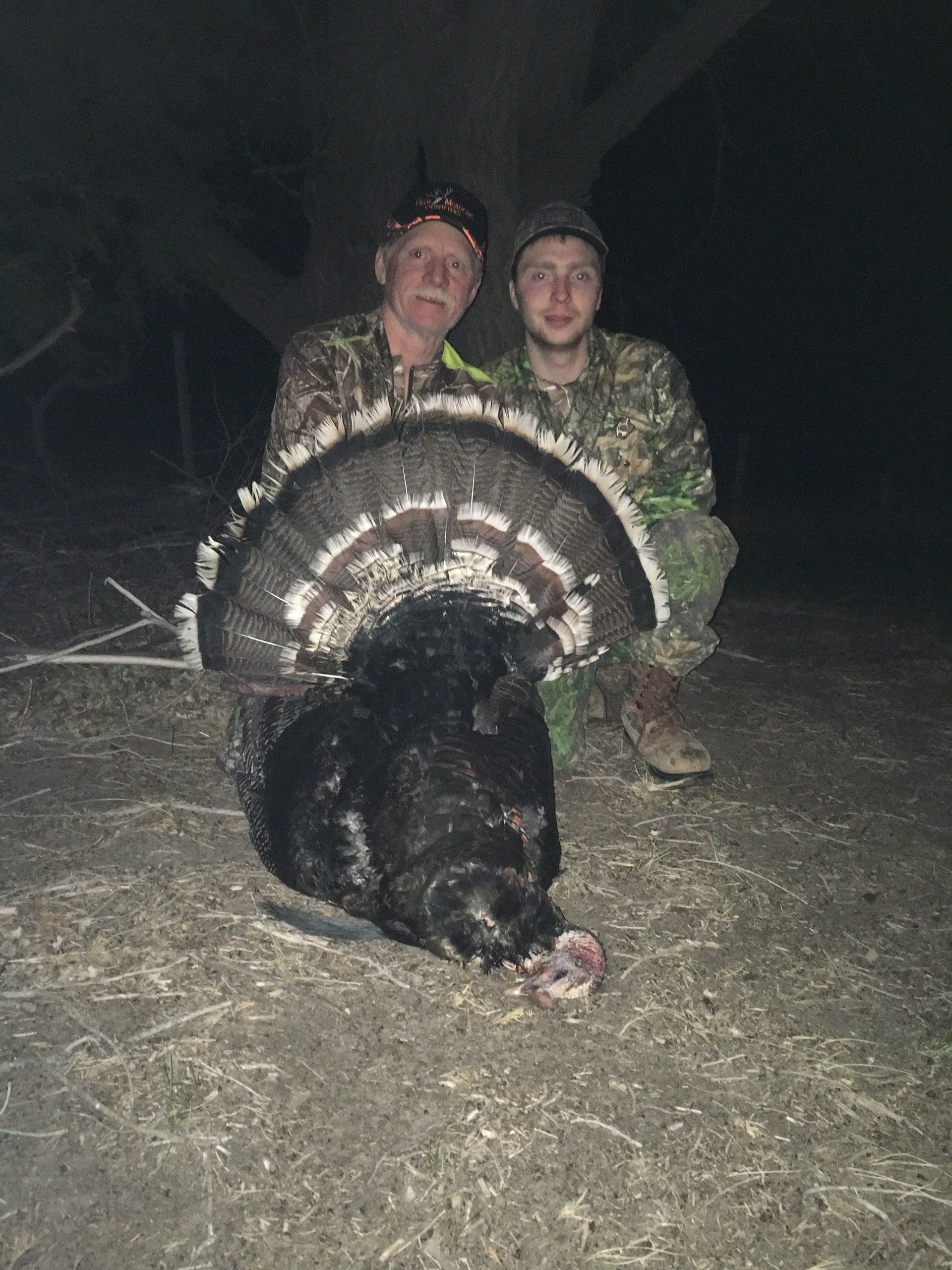 Two people in camo with a harvested turkey. Night setting.