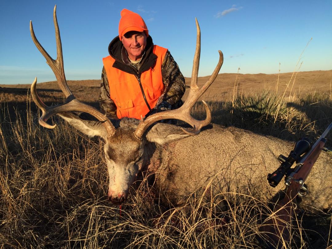 Hunter in orange vest poses with a large buck in a field.