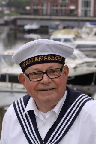 A smiling person wearing a white sailor uniform and a cap with 