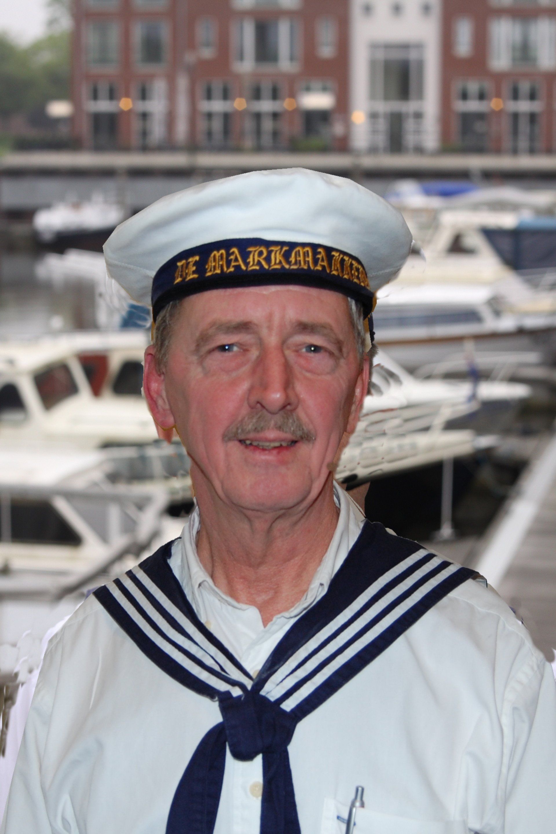 A person wearing a sailor hat and scarf standing in front of a marina with boats and buildings in the background.