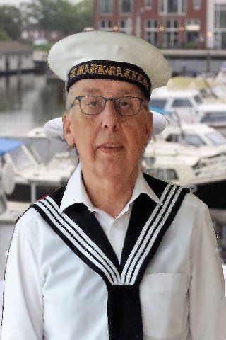 A person wearing a white sailor hat and a traditional navy blue and white collared sailor uniform at a marina.