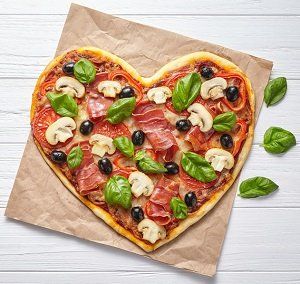 Hartvormige pizza met toppings zoals champignons, olijven en basilicum op bruin bakpapier.