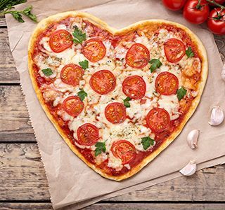 Hartvormige pizza met tomaten en kaas op bakpapier, omringd door tomaten en knoflook.
