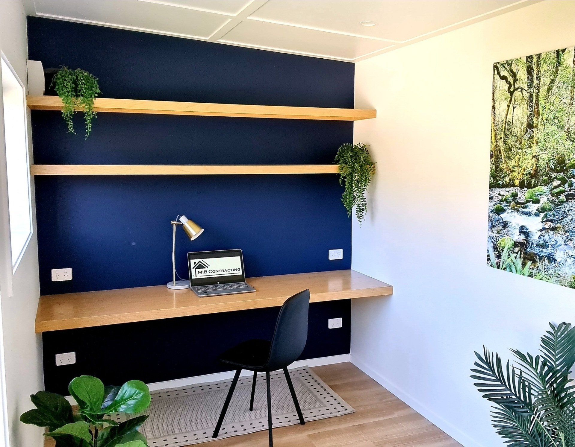A small room with a desk , chair , lamp and shelves.