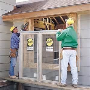 Two men are installing a window on the side of a house.