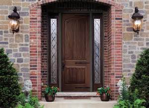 A brick building with a wooden door and two lights on the side.