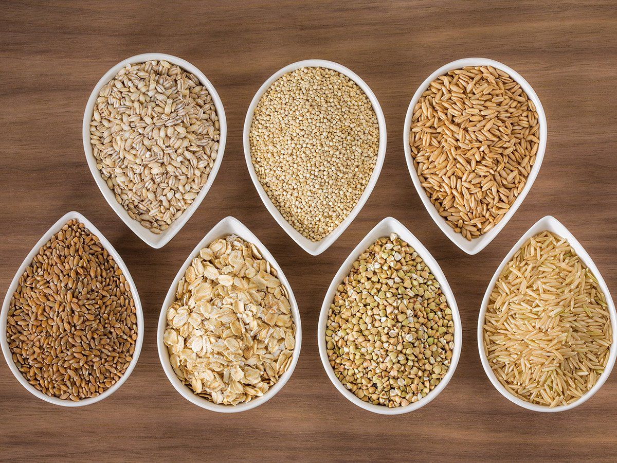 Bowls of various grains and seeds arranged on a wooden surface.