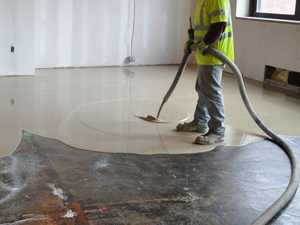 Worker using a vacuum hose to clean a glossy floor in a room under construction