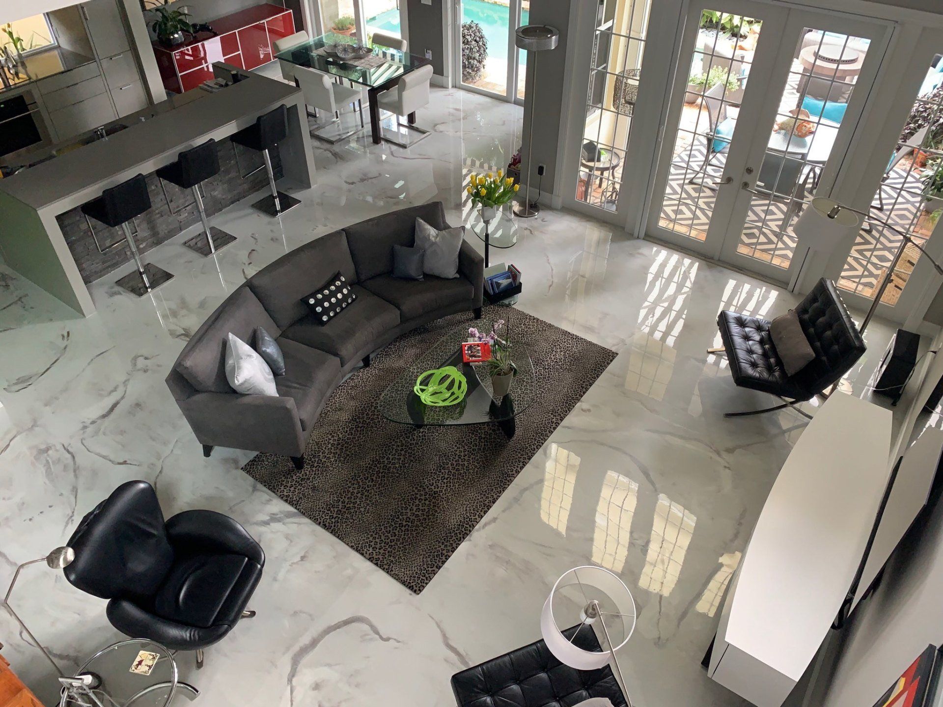 Modern living room with gray sofa, black chairs, rug, and large windows by a glass entryway