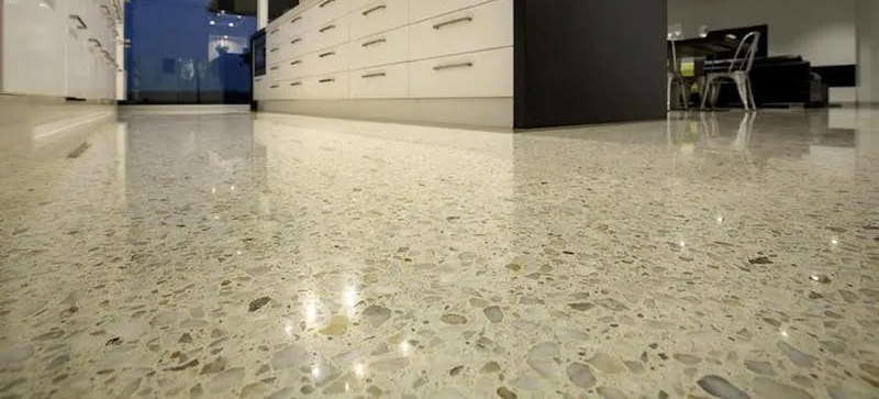 Low-angle view of a polished speckled floor in an office or workshop hallway, with cabinets and chairs in the background