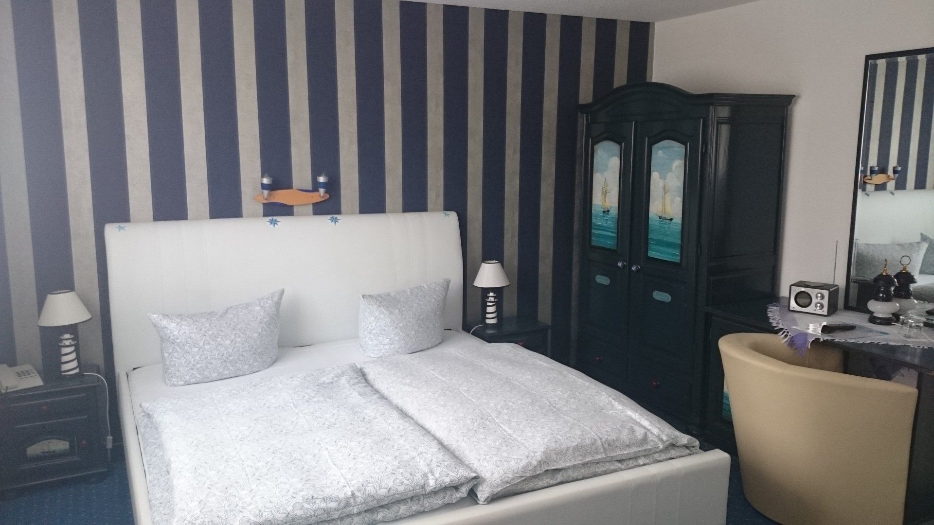 Ein Schlafzimmer mit Bett, Stuhl, Schreibtisch und gestreiften Wänden.