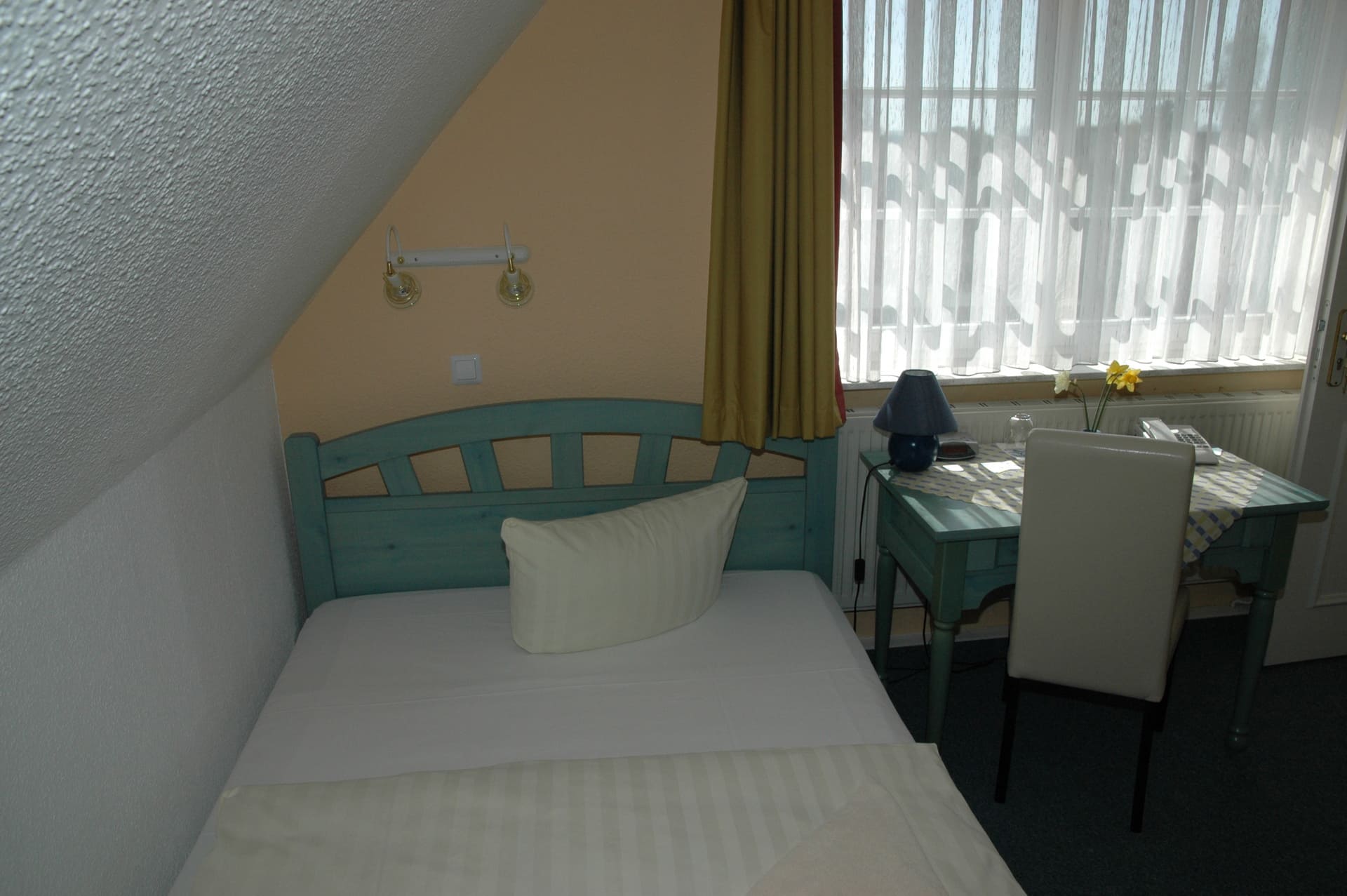Ein kleines Schlafzimmer mit Einzelbett, Schreibtisch, Stuhl und Fenster.