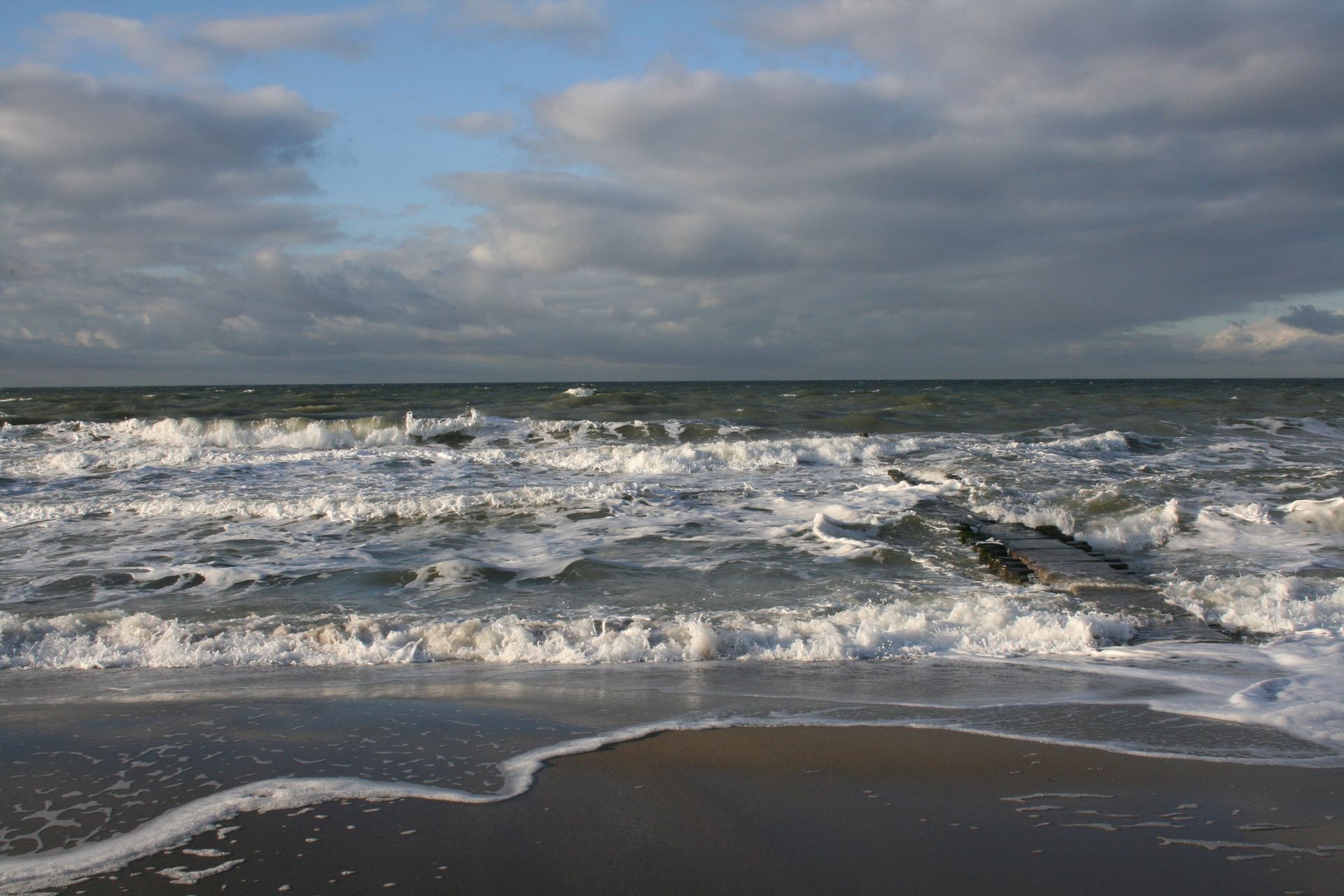 Wellen brechen an einem Strand an einem bewölkten Tag
