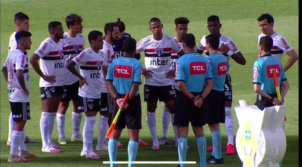 Um grupo de jogadores de futebol e árbitros está em um campo.