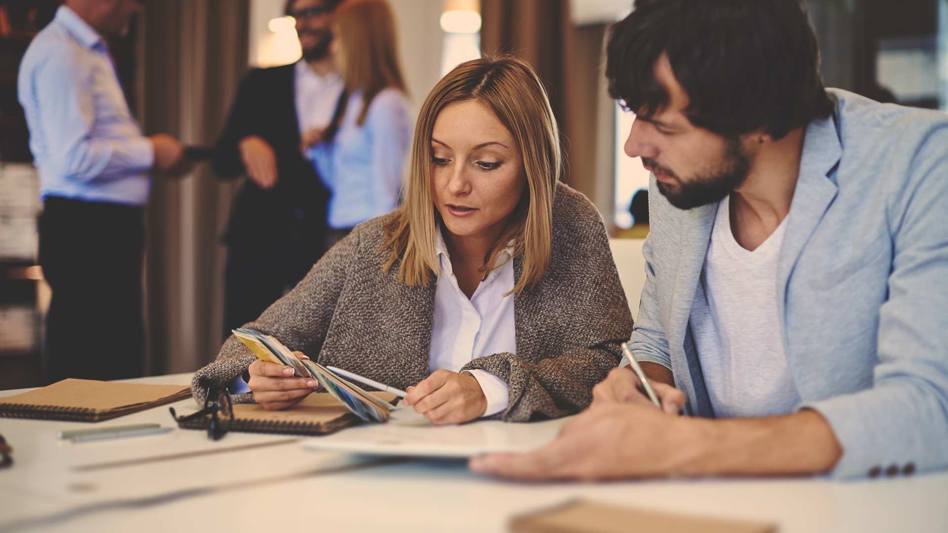 Um homem e uma mulher estão sentados à mesa olhando uma revista.