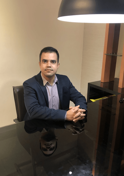 Um homem de terno está sentado à mesa com as mãos cruzadas.