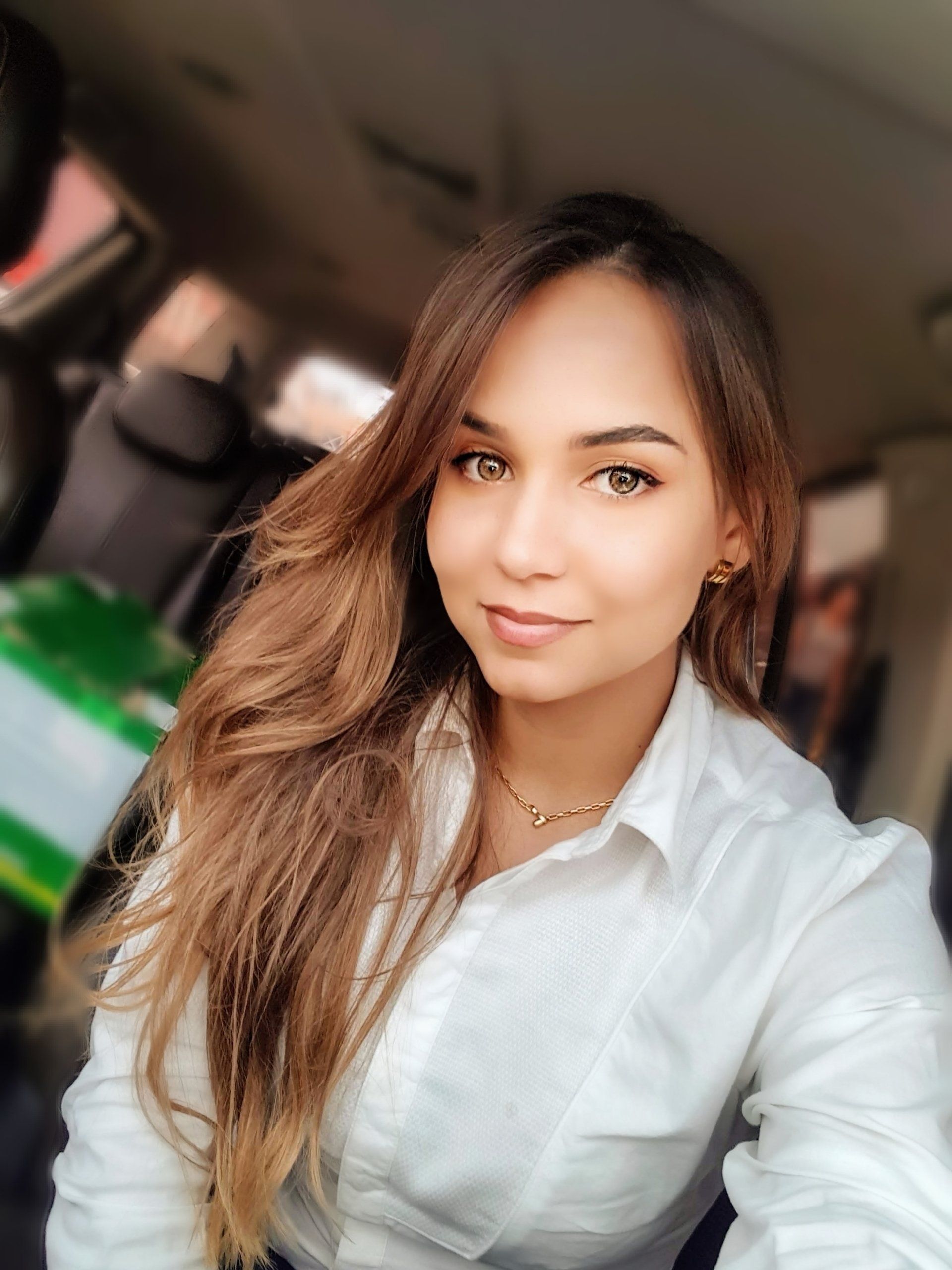 Uma mulher de camisa branca está tirando uma selfie em um carro.