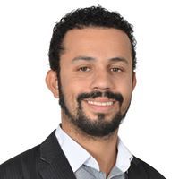 Um homem com barba está vestindo terno e sorrindo.