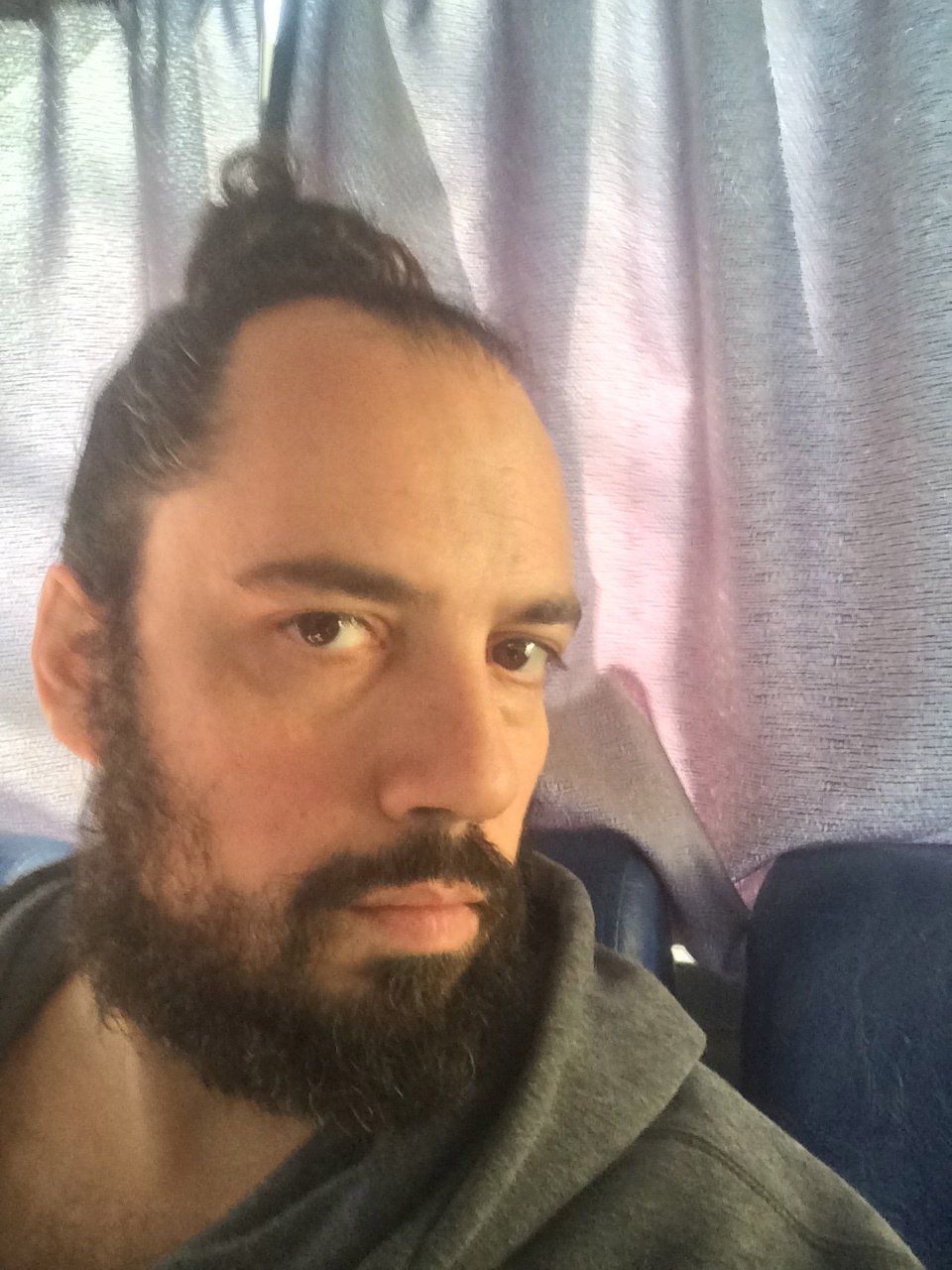 Um homem com barba e coque está sentado em um ônibus.