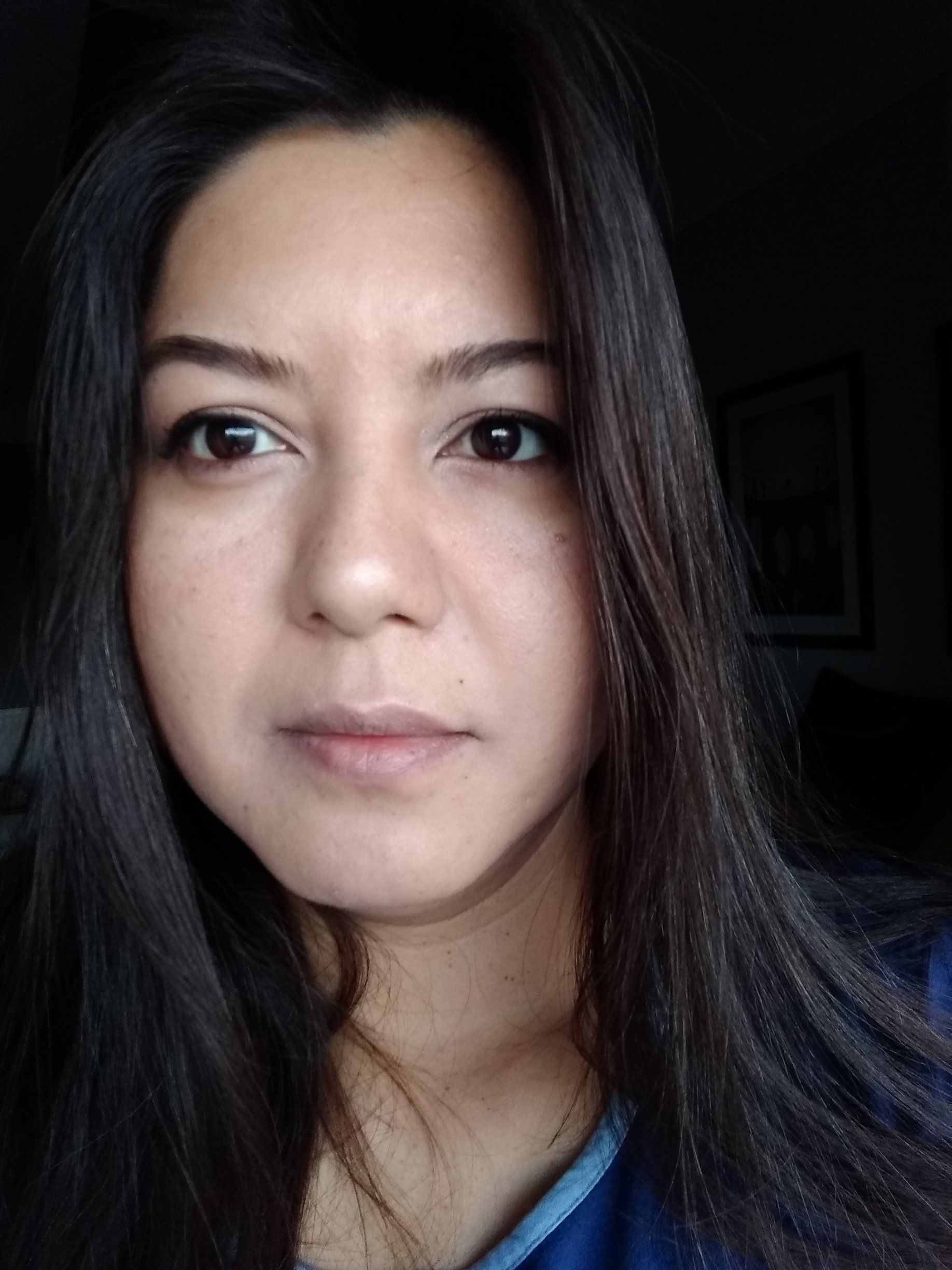 Uma mulher com longos cabelos escuros está vestindo uma camisa azul e olhando para a câmera.