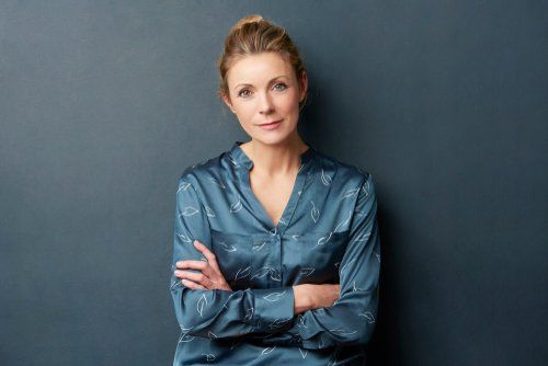 Uma mulher de camisa azul está de pé com os braços cruzados.