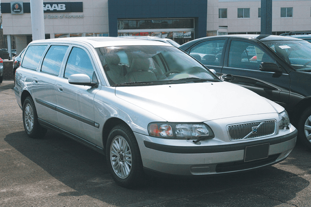 Silver station wagon parked in a lot beside a dark car, with a building in the background