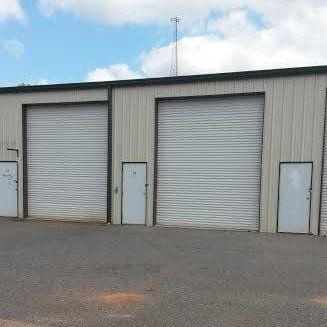 Three gray metal storage units with closed roll-up doors. Small white doors are on the side.