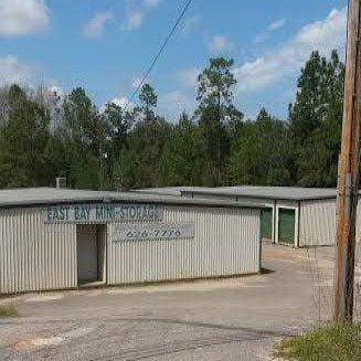 East Bay Mini-Storage building, exterior shot, with tan siding, green doors, blue sky, and trees.