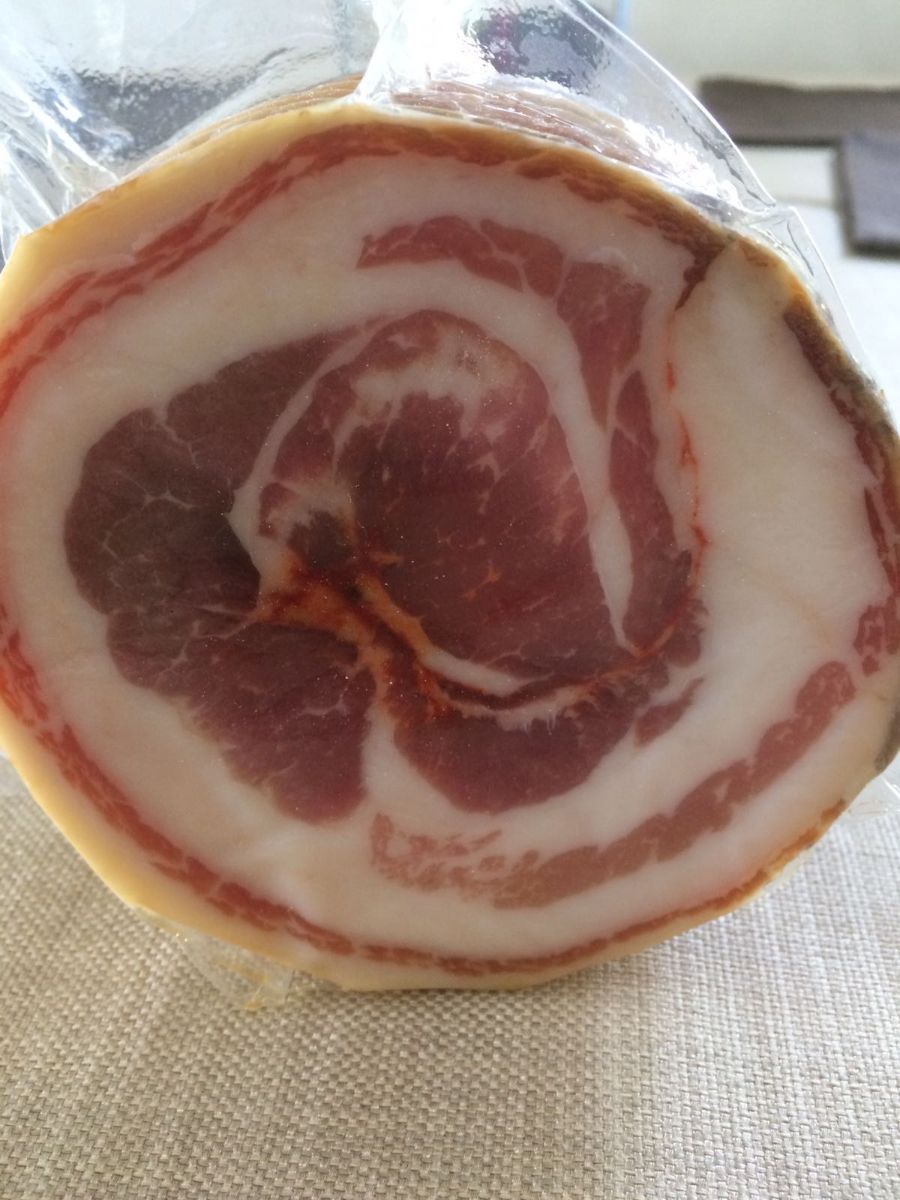 Sezione trasversale di un rotolo di salume con venature rosa e bianche su una tovaglia.