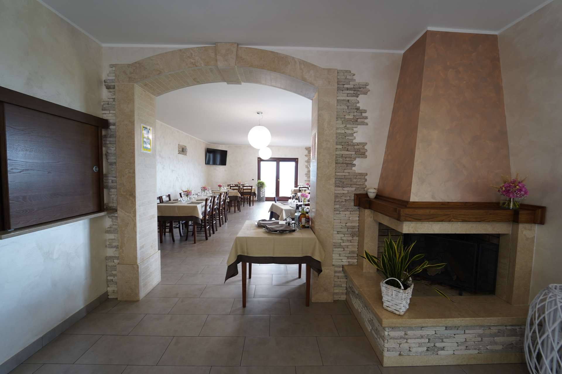 Ampia sala da pranzo con arco in pietra, camino, pavimento piastrellato e tavolo apparecchiato per gli ospiti.