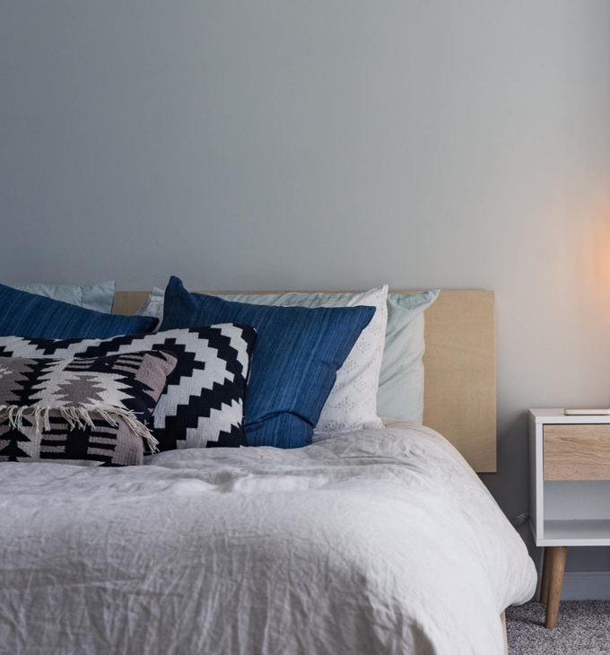 In una camera da letto minimalista, il letto è ben rifatto con cuscini a fantasia blu e nera accanto a un comodino bianco.