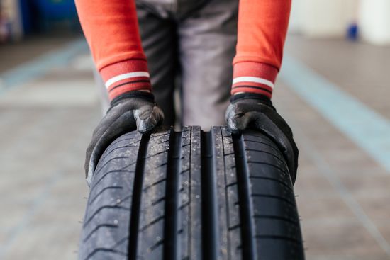 Mechanic Hands Pushing A Black Tire — Lithonia, GA — Martin Tire Co Mechanic Hands Pushing A Black Tire — Lithonia, GA — Martin Tire Co