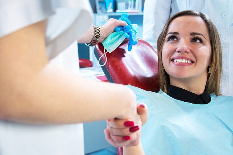 A woman is sitting in a dental chair shaking hands with a dentist.