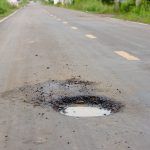 A road with a pothole containing a small amount of water indicates a road maintenance issue