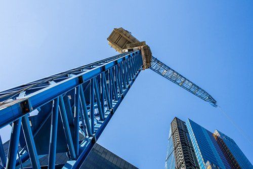 Blue construction crane towers over a modern skyscraper on a clear, sunny day.