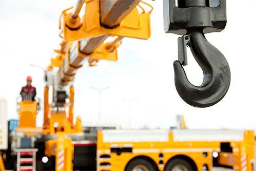Yellow crane with black hook, worker in the cab, clear sky.