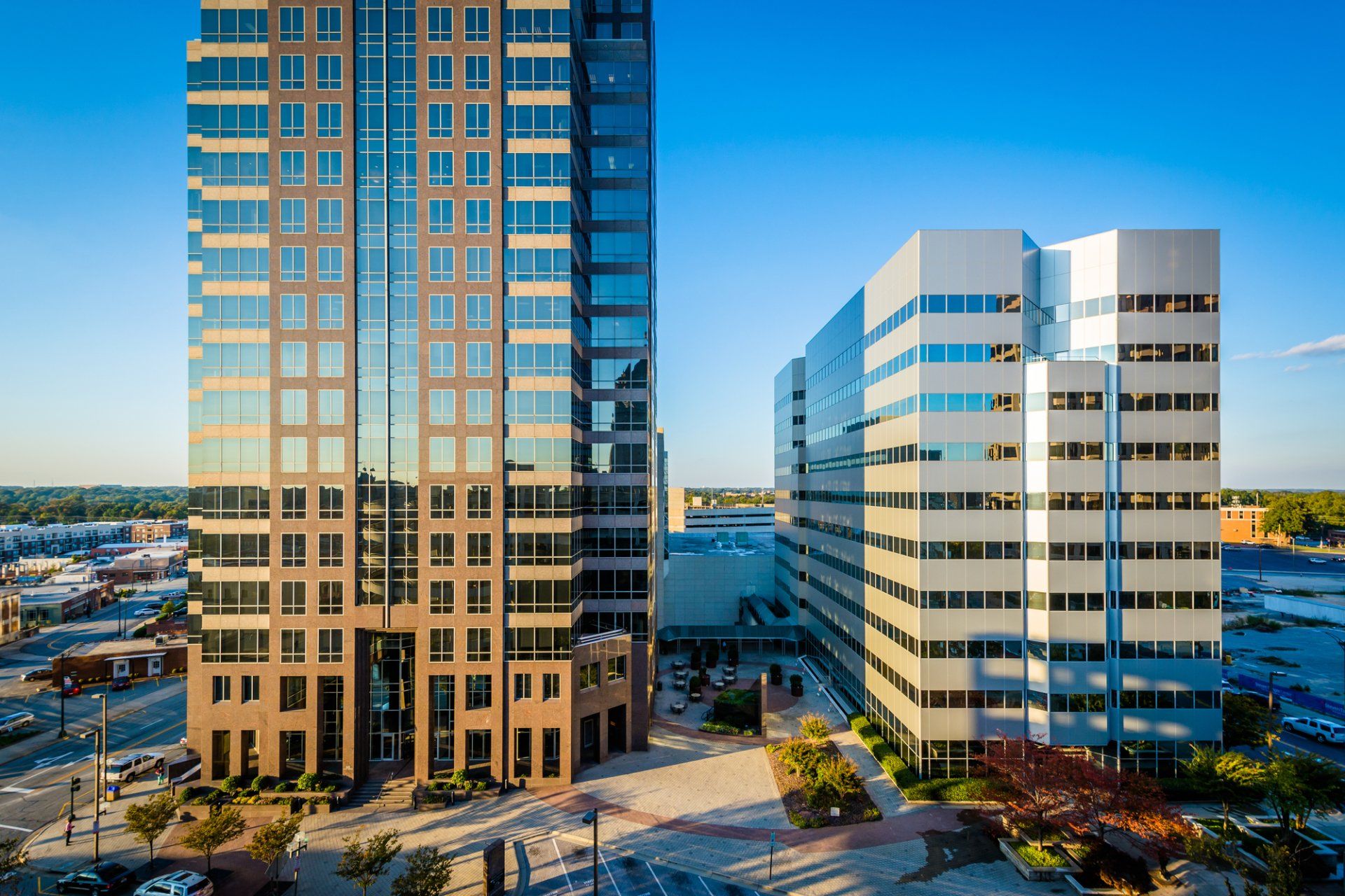 Two modern office buildings against a blue sky; one dark, tall, and one shorter and white.
