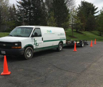 White van with attached trailer, orange cones set up in parking lot.