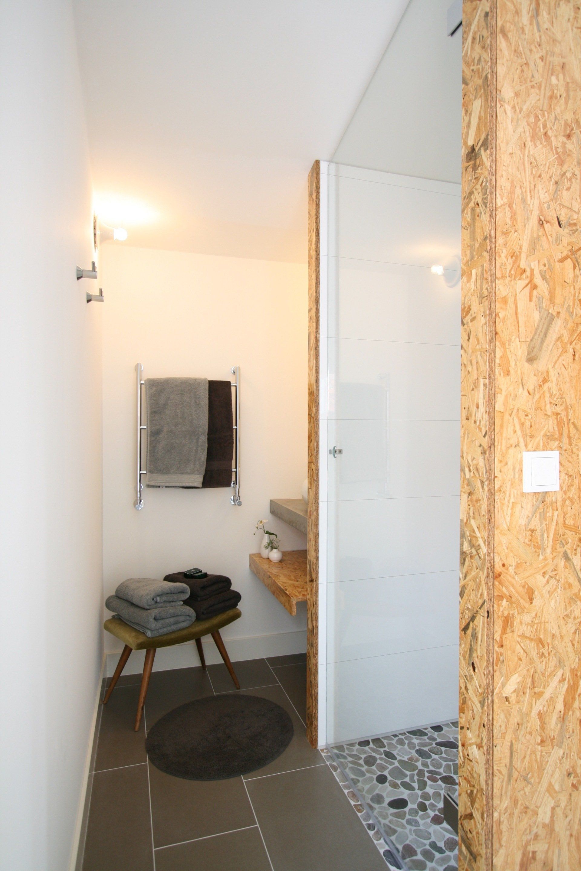 Badkamer met houten accenten, glazen douchecabine en grijze en zwarte handdoeken.
