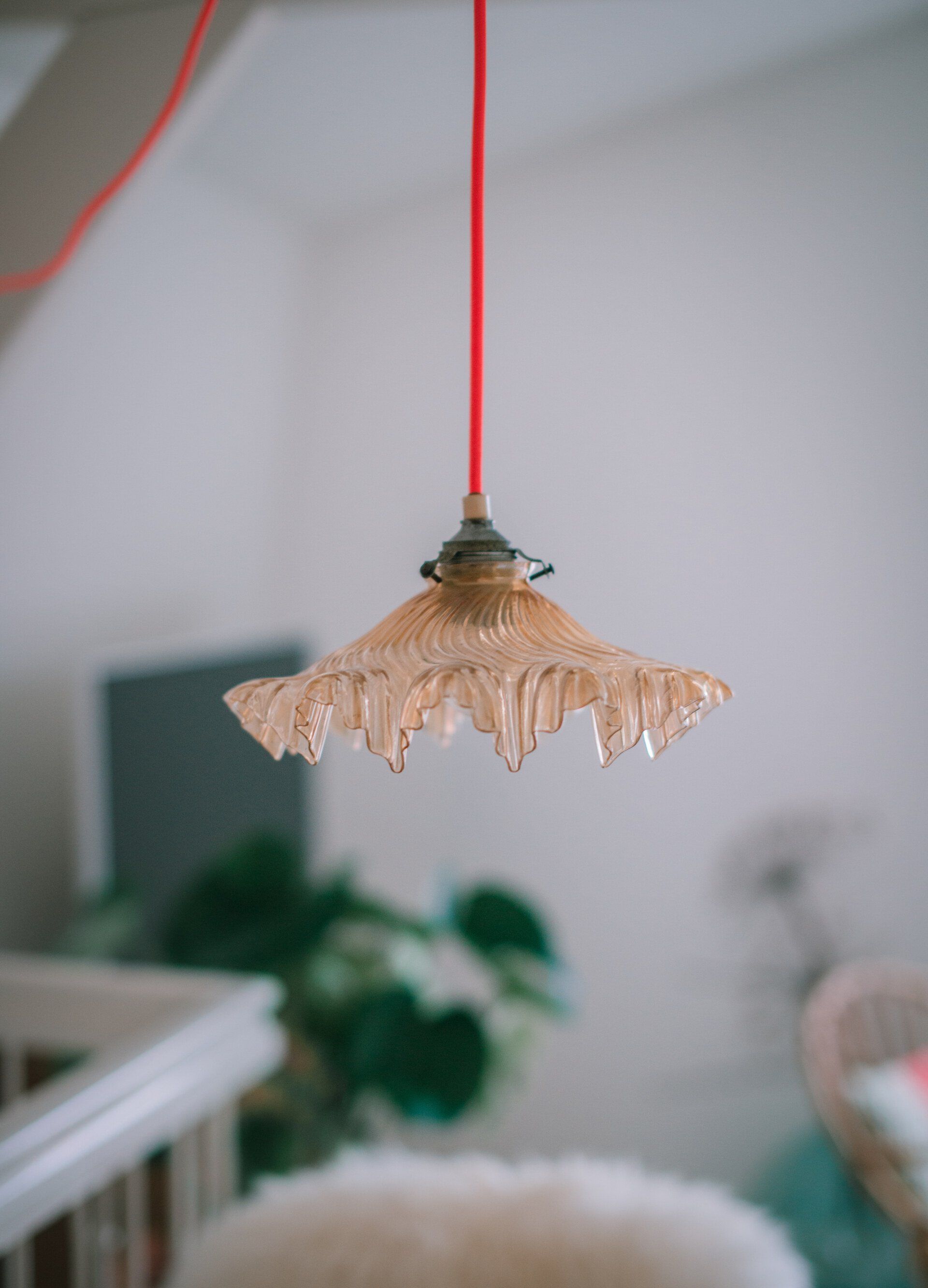 Een oranje glazen hanglamp met rood snoer hangt in een kamer.