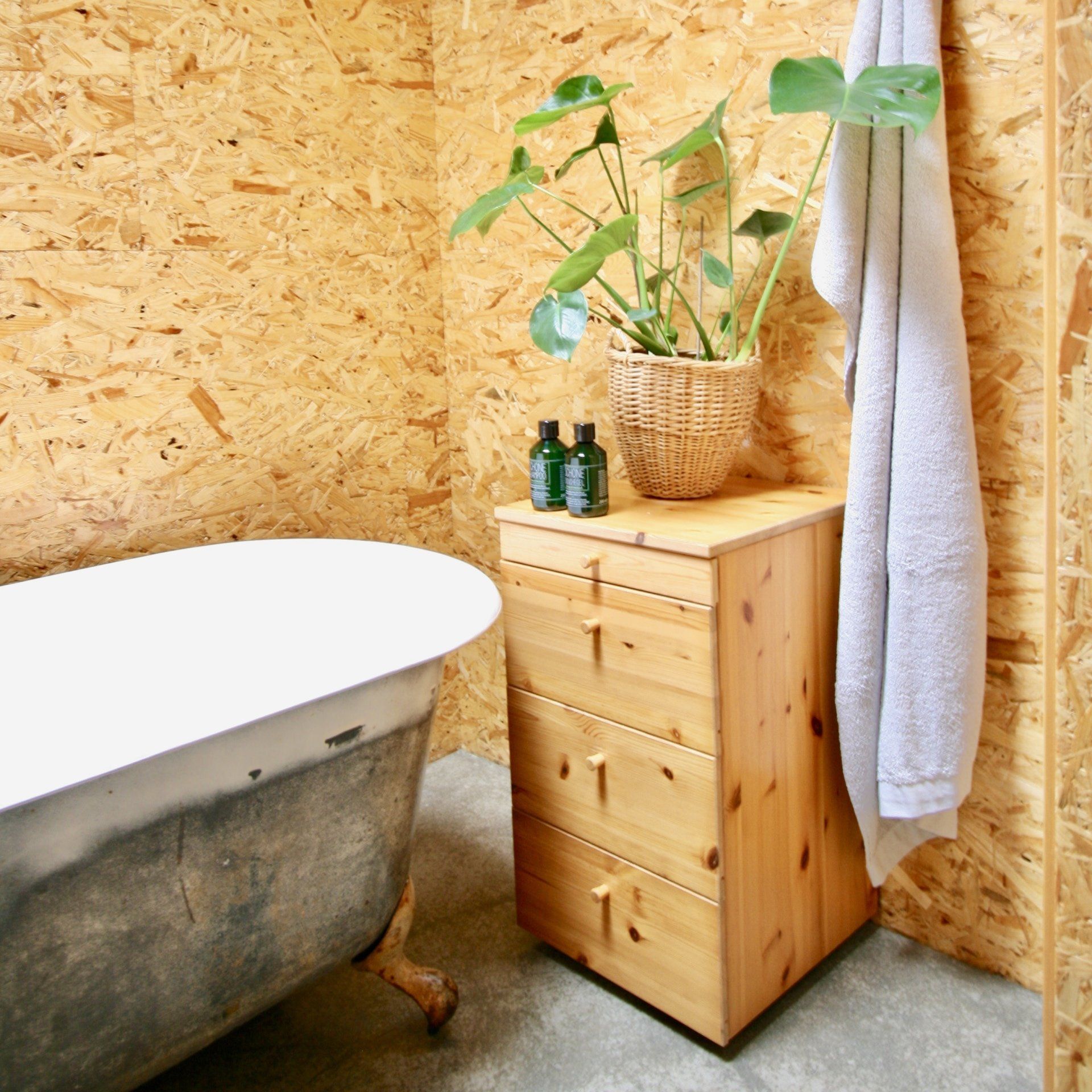 Badkamer met vrijstaand bad op pootjes, houten kast, potplant en handdoek. De wanden zijn bekleed met houten panelen.