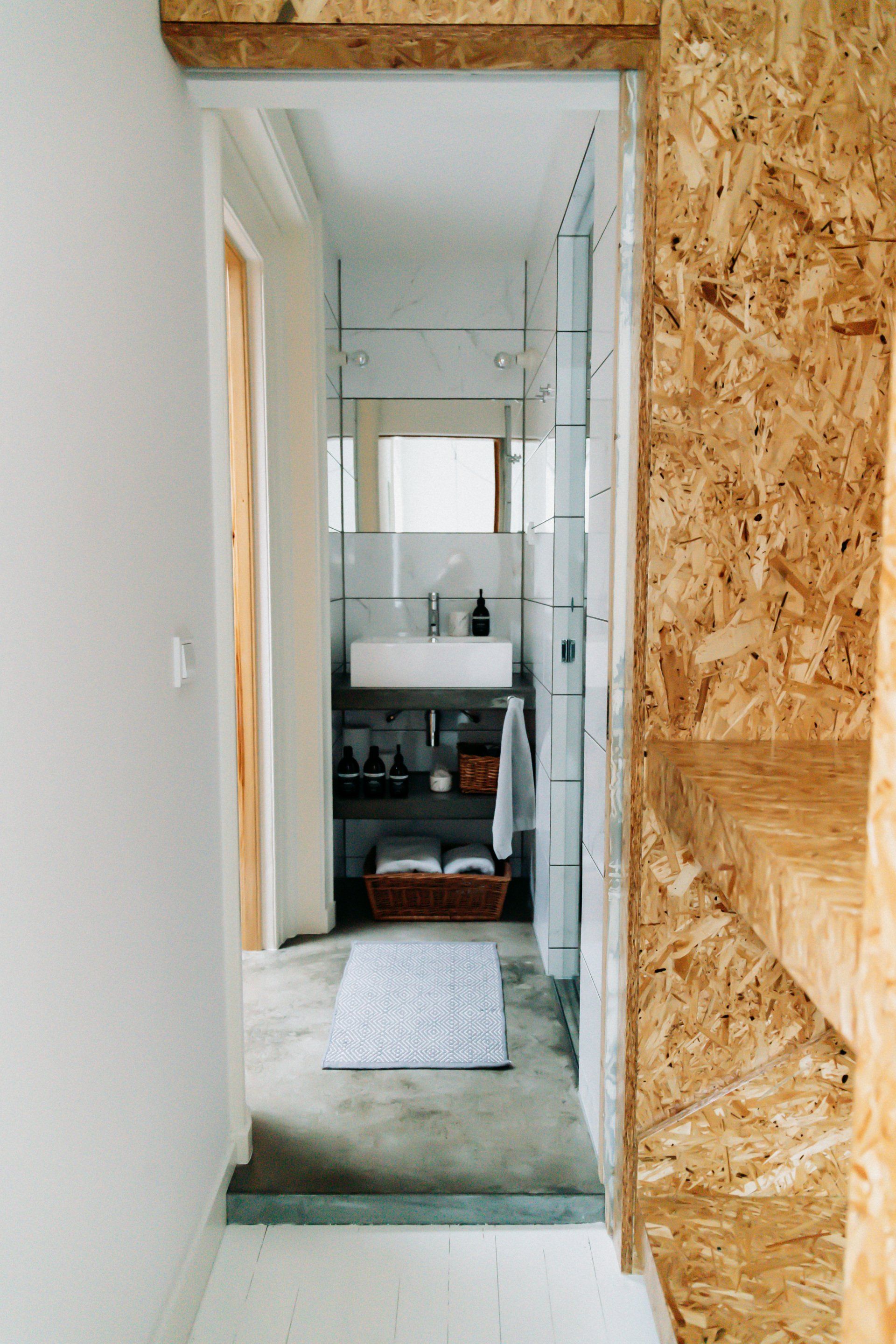 Badkamer met OSB-wanden, betonnen vloer, witte wastafel en glazen douchecabine.