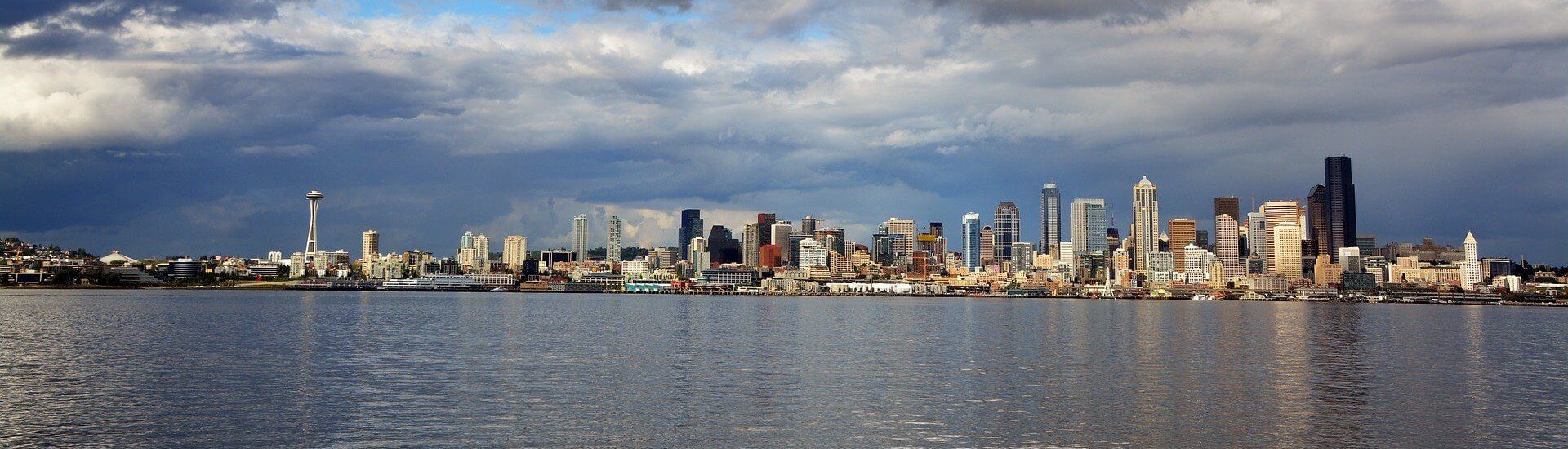 A city skyline is reflected in the water on a cloudy day.